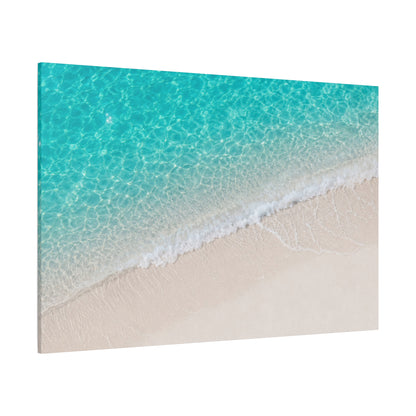 A rectangular wall art print or canvas showing an aerial view of turquoise ocean water meeting pale beige sand, photographed against a plain white background.