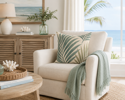 Beige armchair with a palm leaf pillow and green blanket in a living room setting.