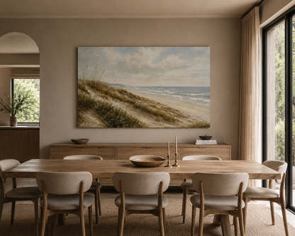 A large rectangular canvas print of a beach dune landscape hangs on a beige wall above a wooden dining table and chairs in a modern dining room.