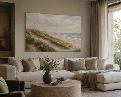A large rectangular canvas painting of a beach dune landscape hangs on a beige wall above a cream sectional sofa in a styled living room.