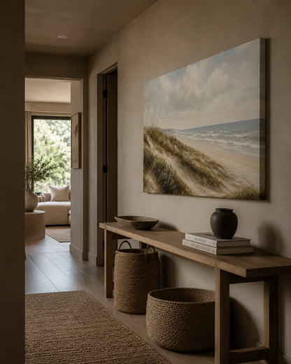 A large vertical canvas print of a beach dune landscape hangs on a beige wall above a wooden console table in a styled interior hallway.