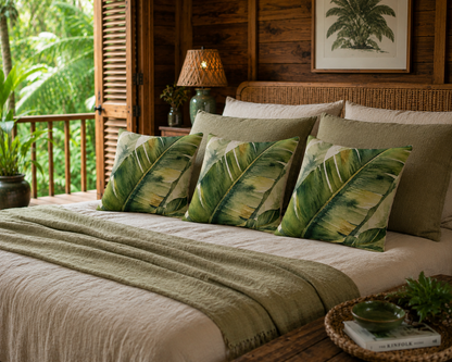A styled bed in a rustic wooden bedroom featuring three decorative throw pillows with a green tropical palm leaf pattern, a beige quilted blanket, and neutral beige bedding.