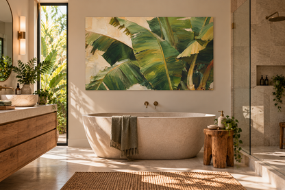 A large rectangular wall art print featuring green banana leaves hangs above a freestanding oval bathtub in a bright, modern bathroom with a wood vanity, glass shower enclosure, and natural light.