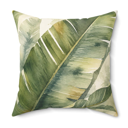 A square decorative throw pillow featuring a watercolor-style print of large green banana leaves on a light cream background, shown against a plain white studio backdrop.